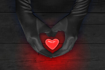 Two hands hold glowing red heart against dark background
