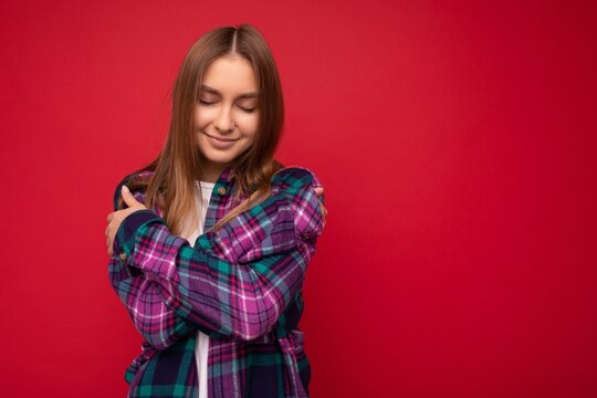 Photo of beautiful cute pretty young blonde woman wearing stylish purple shirt isolated over red background with close eyes and hugging yourself