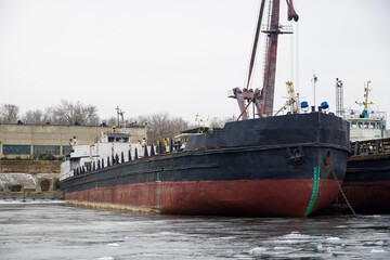Fototapeta premium Old rusty motor ship. Wintering ships on a frozen river in their port. Volgograd. Russia.