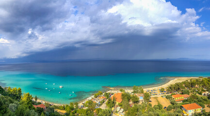 Fototapeta premium Panoramic shot at Chalkidiki Greece at summer 2020 during pandemic covid-19 nice blue sea and the village of Athitos on the coast, and some clouds in the sky 