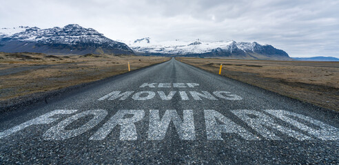 Keep moving forward text quote written on asphalt road leading towards infinity and mountain...