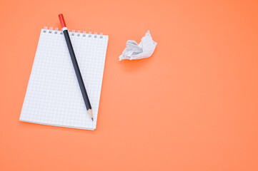 Overhead shot of a pencil on a grid notepad and a crumpled paper isolated on an orange background