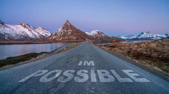 im possible text quote printed on asphalt road towards the mountains during blue hour.