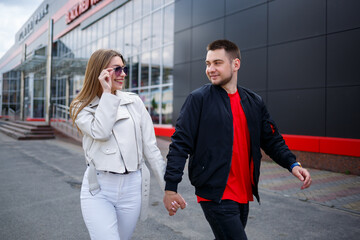 Stylish young girl with blond hair of European appearance and a guy in a black jacket. Urban walk of a couple in love, modern fashion in casual style. Happy relationship concept