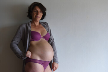 Fototapeta premium a pregnant woman leaning against the wall looking at camera