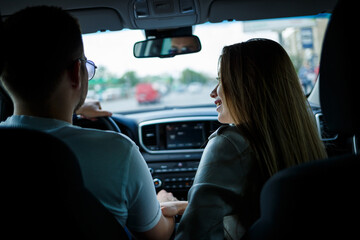 Loving couple in a car hug and hold hands while traveling. Stylish young girl with blond hair of European appearance and a guy in a white polo. Happy relationship concept