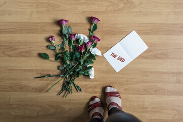 Woman legs in red high heel shoes standing near paper with the end word on a floor with withered flowers. Concept.
