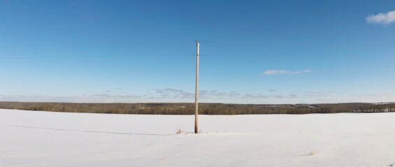 A power pole one an empty snow-covered field in winter