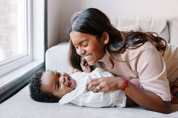 Happy smiling laughing Indian mother playing with black baby girl daughter. Family mixed race...