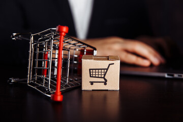 Box with trolly next to laptop. Online shopping concept.