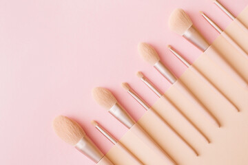 Makeup brushes on pink and beige background. Woman beauty accessory in pastel colors. Flat lay, top view, copy space