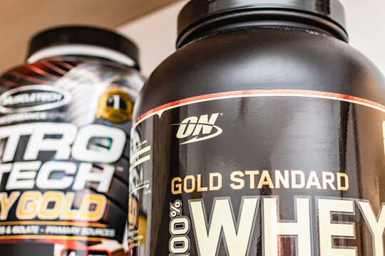 Pote de Whey Protein da marca Optimum Nutrition - 100% Whey Gold Standard e Whey Protein da marca Muscletech ao fundo. Suplemento alimentar, prote&iacute;na, ganho de massa muscular.