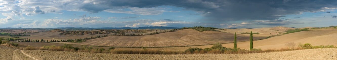Panorama of Tuscan hills and badlands in Val d'Orcia, near Siena medieval town in Tuscany, Italy, with cypress trees, cultivated crop hills and farm houses in the countryside.