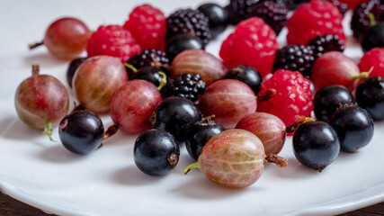 Assorted berries of raspberries, gooseberries, currants on a white plate