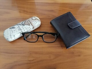 Billetera con lentes de aumento y estuche sobre mesa de madera 