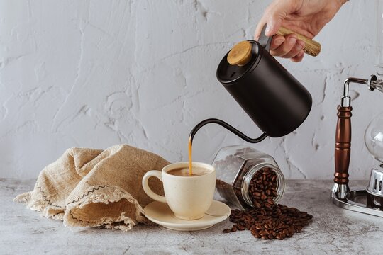 Sirviendo caf&eacute; en una taza desde una cafetera con granos de caf&eacute;