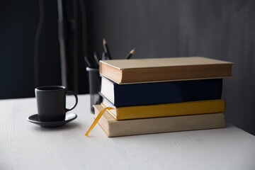 on a white table 4 books next to a black cup