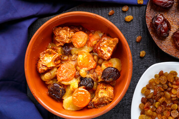 Jewish cuisine dish sweet tsimes with dates, carrots and turkey meat in a brown plate on a blue background near raisins and dates.