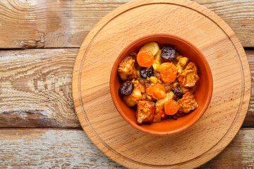 A dish of Jewish cuisine tsimes with carrots, dates and turkey meat in a clay plate on a wooden round stand top view.