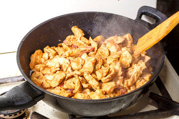 Chicken fillet in soy sauce with lemon juice stirring a wooden spatula in a frying pan.