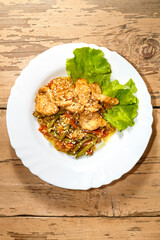 Vegetables with rice and chicken in Pan-Asian sauce and sesame seeds on salad leaves on a wooden table in a plate.