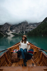 Happy tourist woman with hat sitting in a wooden boat on Braies lake surrounded by the mountains of the Italian Alps 