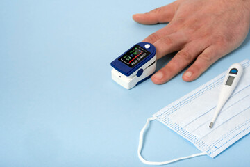 Human male hands pulse oximeter used to measure pulse rate and oxygen levels with medical blue...