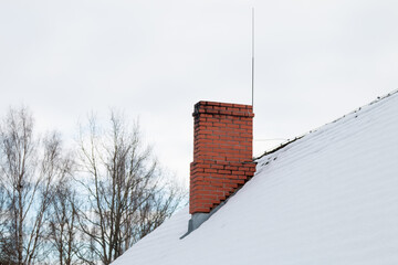 Red brick chimney on a snowy roof in winter