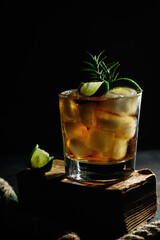 Alcoholic cocktail with ice whiskey. Cocktail with lime and rosemary in a glass on a dark background. Dark photo