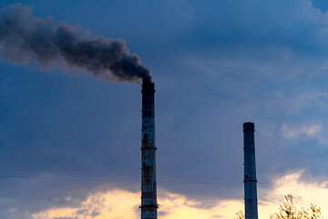 Factory pipes and white smoke floating in the air. Industrial tube and smoke from chimney with cloudy cold day on the background.