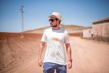 Young man in a straw hat walking down a dusty dirt road next to a plowed field