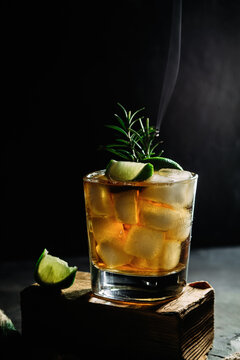Alcoholic cocktail with ice whiskey. Cocktail with lime and rosemary in a glass on a dark background. Dark photo
