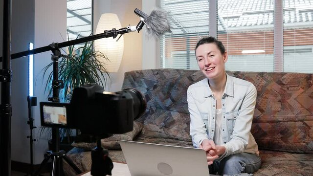 Woman blogger or vlogger streaming online on social media to her subscribers. Woman using microphone, video camera and other blogging set ups at her house while talking on camera.