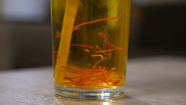 Wooden stick mixing saffron crimson stripes in a glass with hot water on table