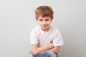 thoughtful sad schoolboy in a white T-shirt on a gray background