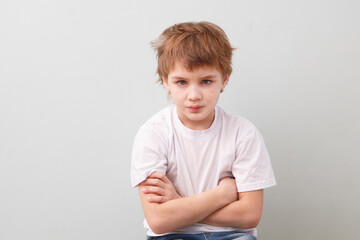 thoughtful sad schoolboy in a white T-shirt on a gray background