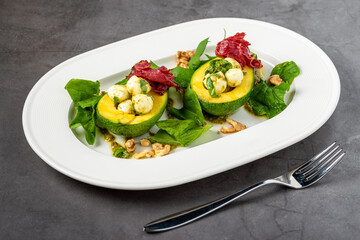 Bocconcini cheese balls in halves of avocado served with salad on white plate