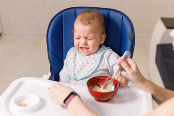 Mother tries to feed with spoon naughty infant kid refusing eating