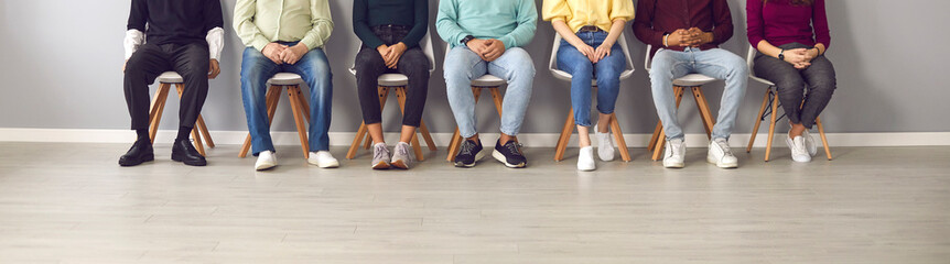 Cropped image of unrecognizable people sitting in the waiting room on chairs in line. Group of...