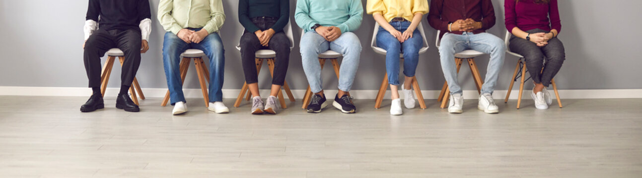 Cropped image of unrecognizable people sitting in the waiting room on chairs in line. Group of unidentified people in casual clothes are waiting their turn for an interview or a doctor's appointment.