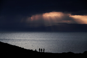 Four people backlit in an oceanfront sunset scene. Sunbeams break through the clouds at sunset. Cabo de Gata Park. Almeria - obrazy, fototapety, plakaty