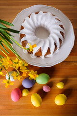 Traditional Easter cake surrounded by colorful eggs and flowers on brown wooden table.
