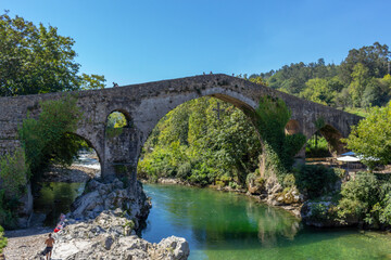 Fototapeta na wymiar Cangas de Onis, Spain - September 4, 2020: The Roman Bridge of Cangas de Onís, the “Puente Vieyu” or “Puentón”. Medieval stone bridge over the Sella River, Asturias, Spain.