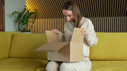 Fototapeta na wymiar Smiling woman sit on sofa at home open cardboard delivery package shopping online