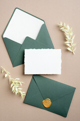 Wedding details card and green envelopes on pastel beige background. Flat lay, top view, copy space.