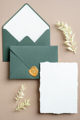 Wedding details invitation template. Minimalist wedding card and green envelopes on pastel beige background with dried flowers. Flat lay, top view.