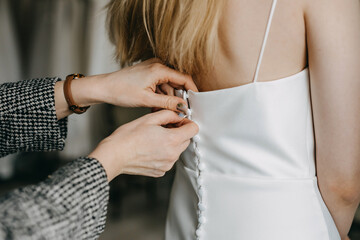 Closeup of a woman buttoning wedding dress back buttons.