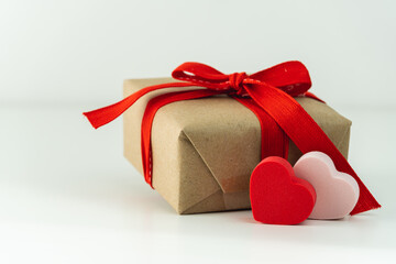 Close-up of gift box with red ribbon and two hearts on white background.