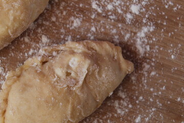 Raw cooking dumplings lie on a board beside egg flour on a pink background view from above