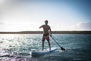 Fototapeta na wymiar a young sportsman man practices paddle surfing on the beach under a blue sky